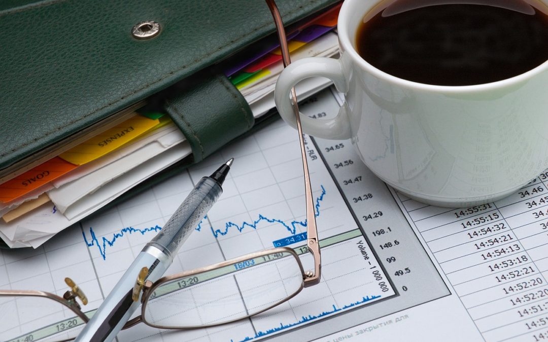 photo of a pair of glasses, a cup of coffee, a pen, a notebook and some charts and graphs